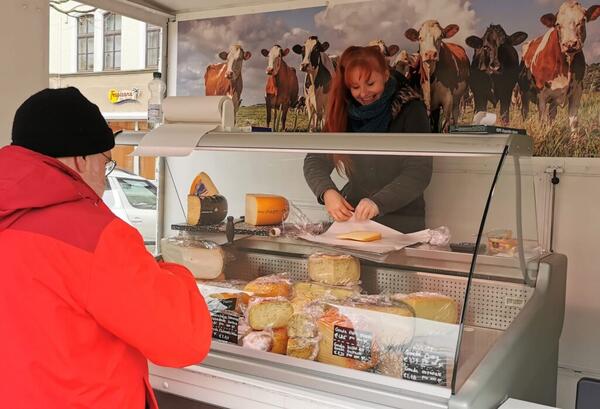 Das Foto zeigt eine Verkäuferin in einem Käsestand, die für einen Kunden gerade Ware abpackt.