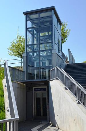 Das Foto zeigt den Fahrstuhl am Bahnhof in Steinheim von der Billerbeckerstraße aus. Die Böschung rechts und Links wird durch Betonwände abgefangen. Von dort kann man dann den Höhenunterschied zum höher gelegenen Bahnhof überbrücken.