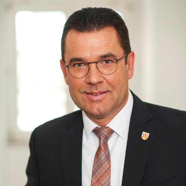 Das Foto zeigt ein Portrait des Bürgermeisters Carsten Torke im grauen Sakko und weißem Hemd mit rot weiß blau quer gestreifter Krawatte.