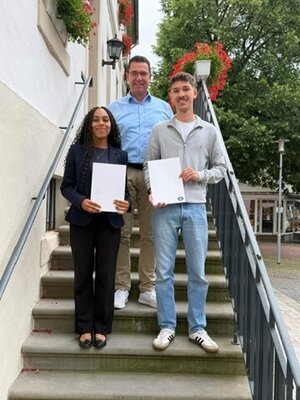 Das Foto zeigt den B&uuml;rgermeister Carsten Torke mit den beiden ehemaligen Auszubildenden Lilli Symalla und Hauke Torke, die stolz ihre Abschlusszeugnisse hochhalten.